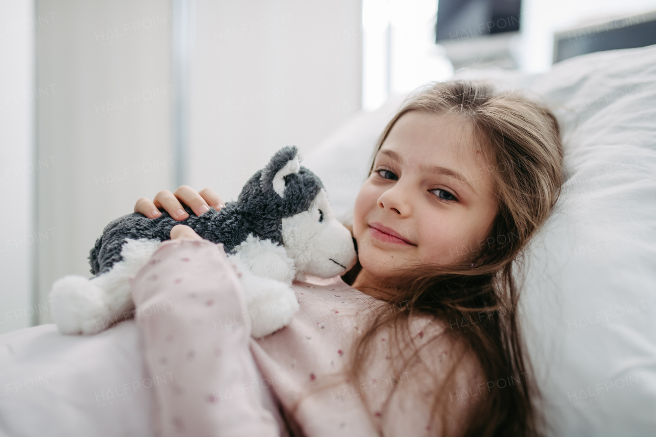 Little girl patient lying in hospital bed. Children in intensive care unit in hospital with plush toy, toy dog.