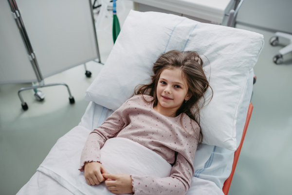 Little girl patient lying in hospital bed. Children in intensive care unit in hospital smiling, feeling better.