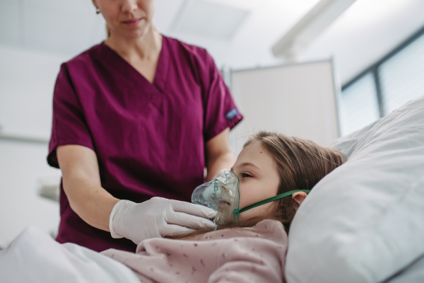 Nurse putting an oxygen mask on a girl's face. Child patient in hospital bed with an oxygen mask on her face.