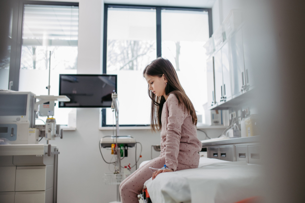 Worried children patient in emergency room, sitting on bed, waiting for doctor. Concept of emotional support and friendliness for young kid patient.