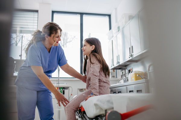 Supportive doctor soothing a worried girl patient in emergency room. Concept of emotional support and friendliness for young kid patient.