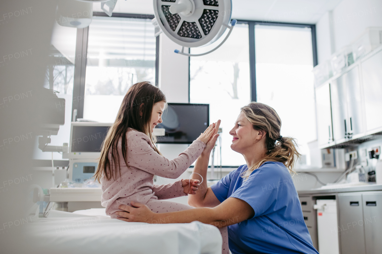 Supportive doctor high five with girl patient in emergency room. Concept of emotional support and friendliness for young kid patient.