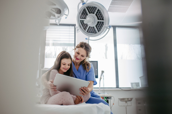 Supportive nurse watching a cartoon on a tablet with children patient to her calm down. Concept of emotional support and friendliness for young kid patient.