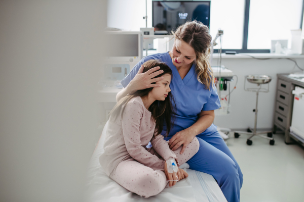 Supportive doctor soothing a worried girl patient in emergency room. Concept of emotional support and friendliness for young kid patient.