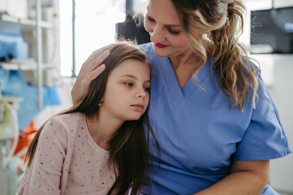 Supportive doctor soothing a worried girl patient in emergency room. Concept of emotional support and friendliness for young kid patient.