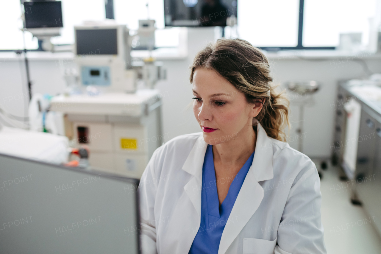 Beautiful female doctor working on laptop in doctor's office. Physician doing paperwork and administrative tasks.