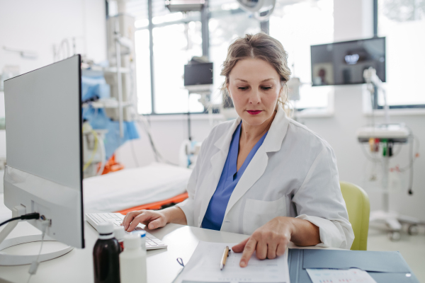 Female doctor working on computer in doctor's office, looking at MRI scan, test results of patient. Doctor consulting scan with the other doctors.