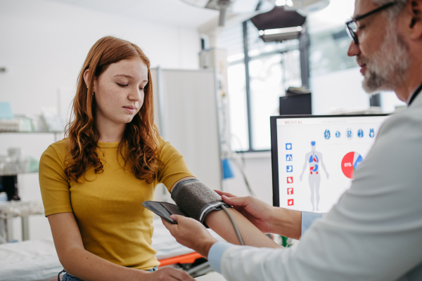 Doctor examining teenage girl, measuring blood pressure, using clinical blood pressure monitor. Concept of annual preventive health care for teenagers.