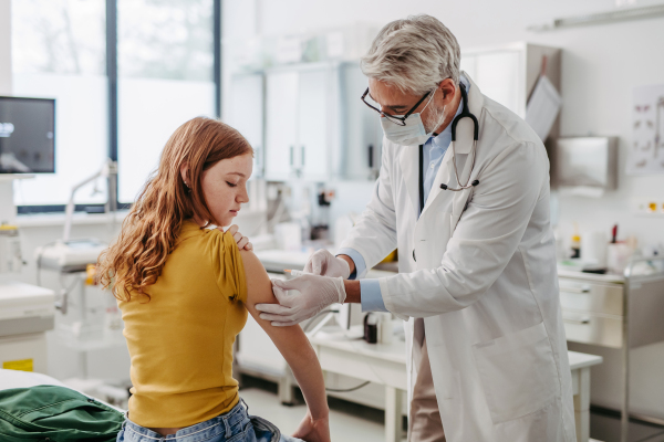 Doctor, pediatrician injecting vaccine into teenage girl arm, routine vaccinations. Concept of preventive health care for adolescents.