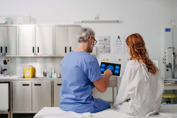 Rear view of doctor showing girl teenage patient MRI scan on tablet, discussing test result in emergency room.