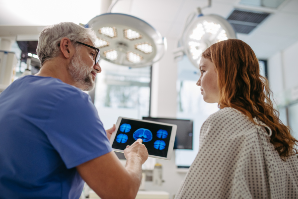 Doctor showing girl teenage patient MRI scan on tablet, discussing test result in emergency room.