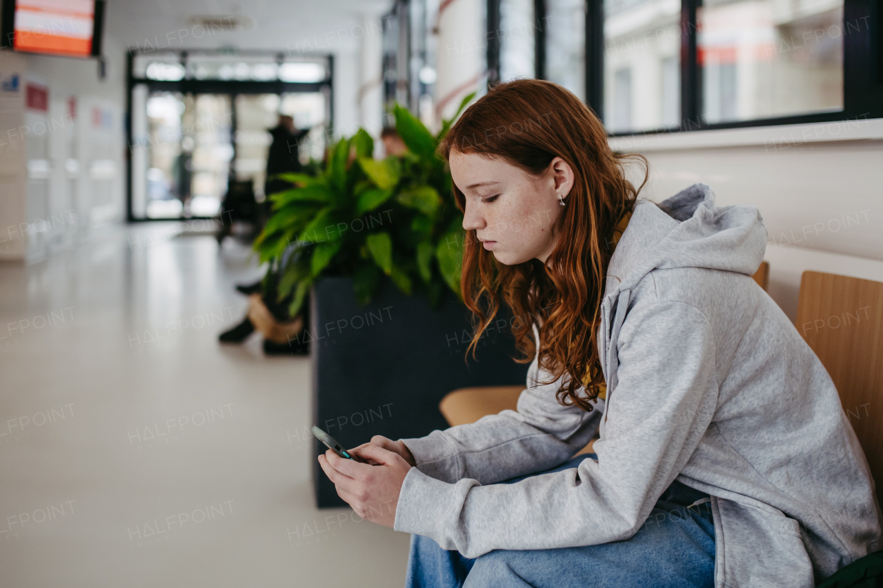 Teenage girl waiting in hospital corridor, listening music via headphones. Adolescent patient coming to hospital for examination.