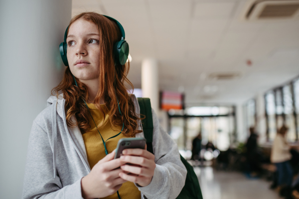 Teenage girl waiting in hospital corridor, listening music via headphones. Adolescent patient coming to hospital for examination.