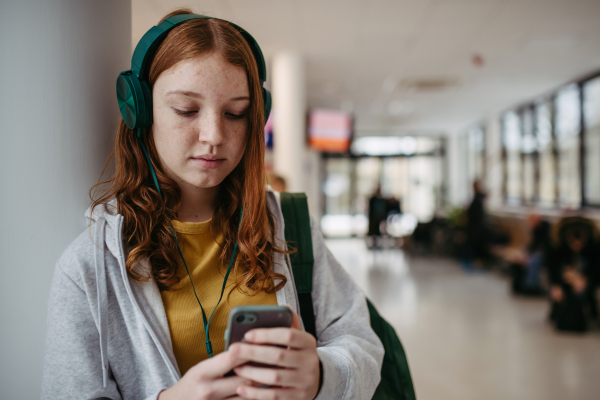 Teenage girl waiting in hospital corridor, listening music via headphones. Adolescent patient coming to hospital for examination.