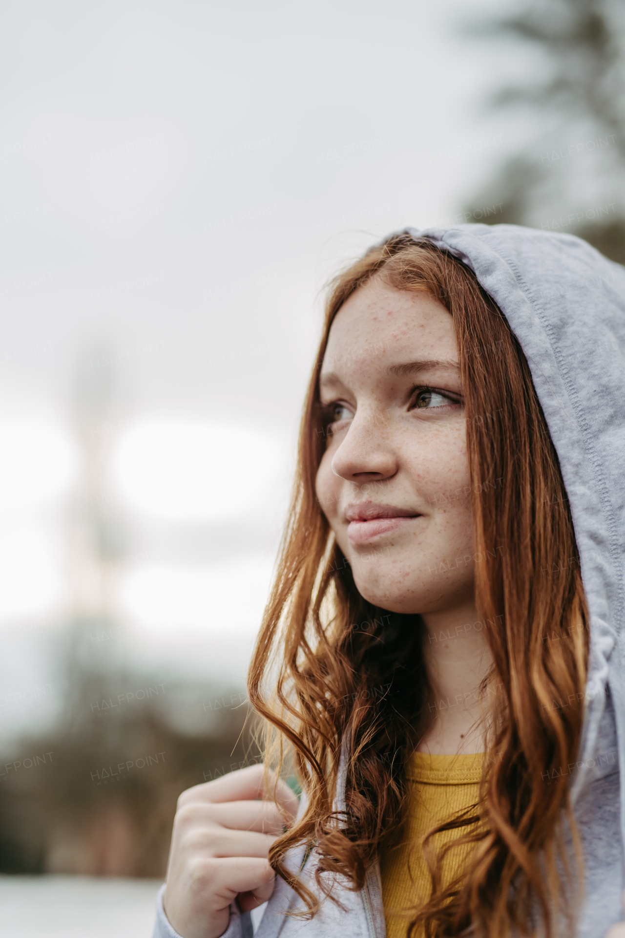 Portrait of beutiful red head gen z girl outdoors. Girl with copper hair, freckles with hoodie on head.