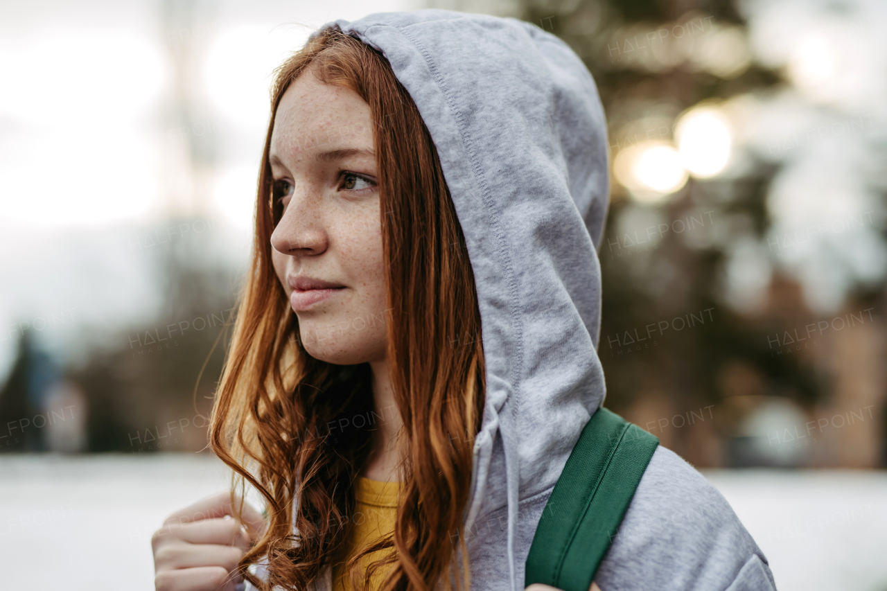 Portrait of beutiful red head gen z girl outdoors. Girl with copper hair, freckles with hoodie on head.