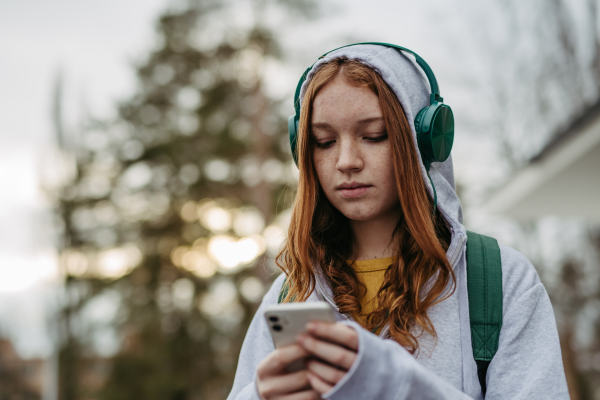 Portrait of teenage girl looking at her smartphone, feeling sad, anxious, alone. Cyberbullying, girl is harassed, threated online.