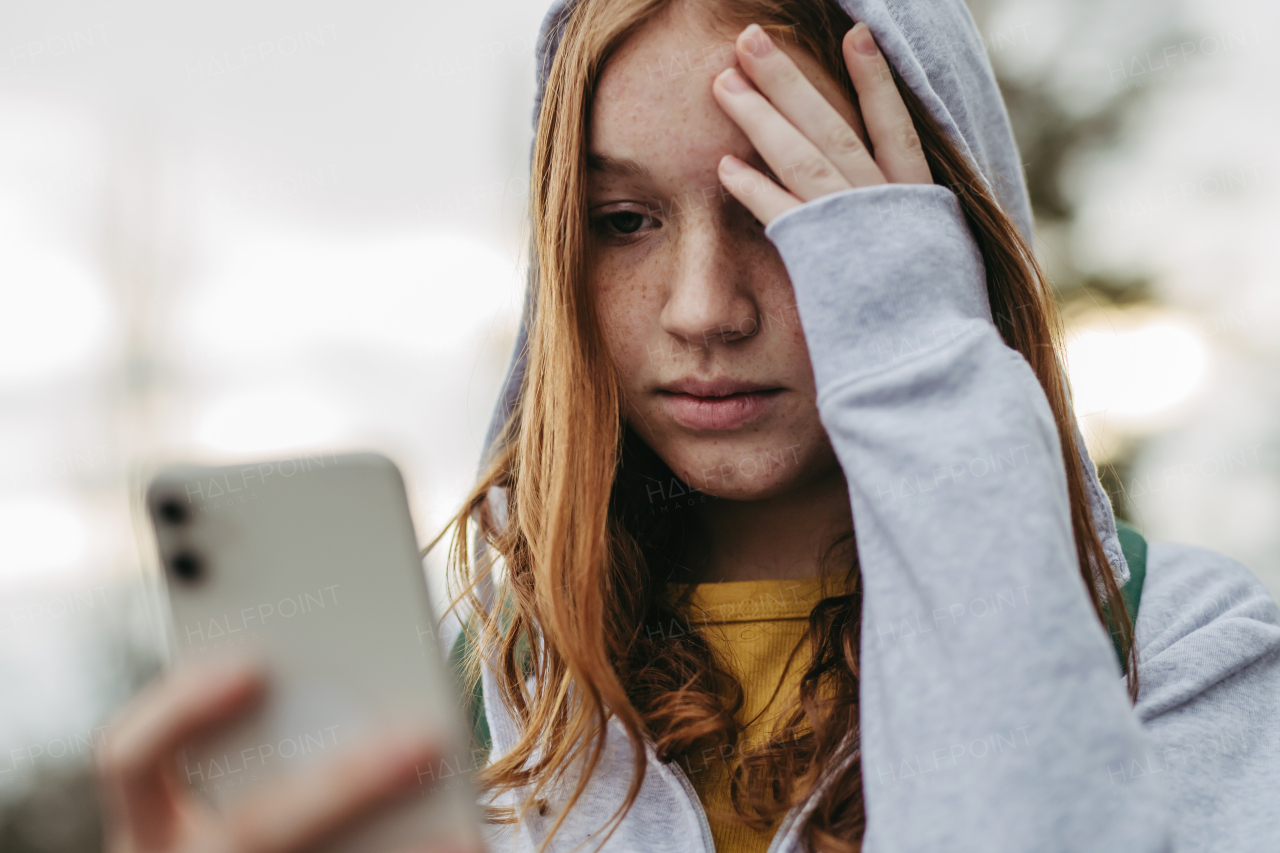 Portrait of teenage girl looking at her smartphone, feeling sad, anxious, alone. Cyberbullying, girl is harassed, threated online.