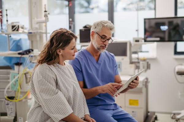 Doctor showing female patient MRI scan on tablet, discussing her test result in emergency room.