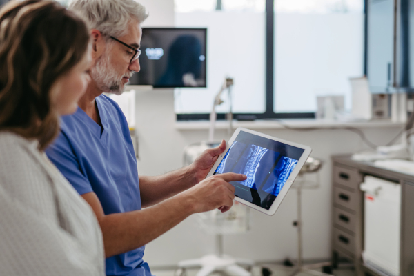 Doctor showing female patient MRI scan on tablet, discussing her test result in emergency room.