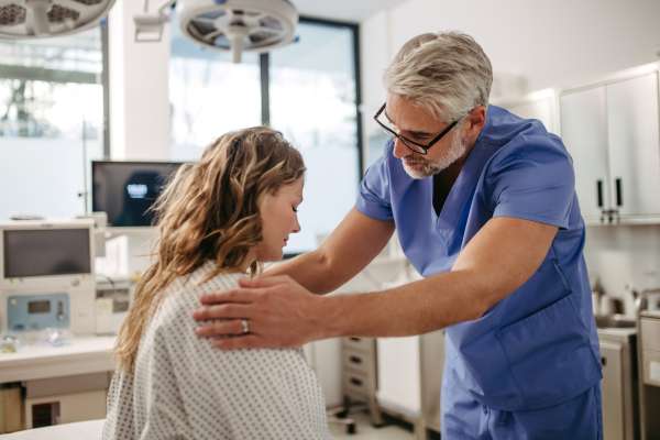 Supportive doctor soothing a worried female patient, discussing test result in emergency room. Compassionate physician supporting stressed patient.