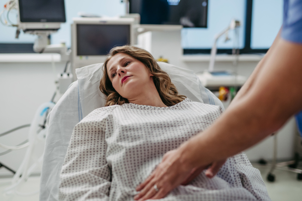 ER doctor palpating woman's abdomen, using hands and steady pressure.