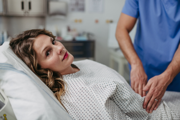 ER doctor palpating woman's abdomen, using hands and steady pressure.