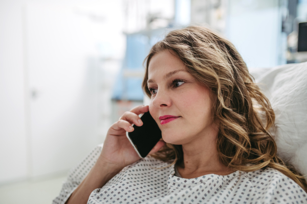 Happy woman phone calling from hospital room after successful surgery. Emotional support from family for patients in hospital.