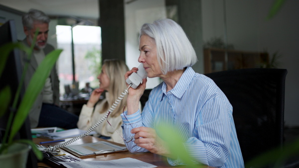 A successful business deal for older manager working in office. Beautiful mature woman making phone call. Age diverse team concept.