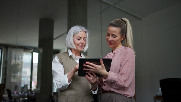 Two female colleagues in various age groups in office. Older manager as mentor for new female employee. Age diverse team concept.