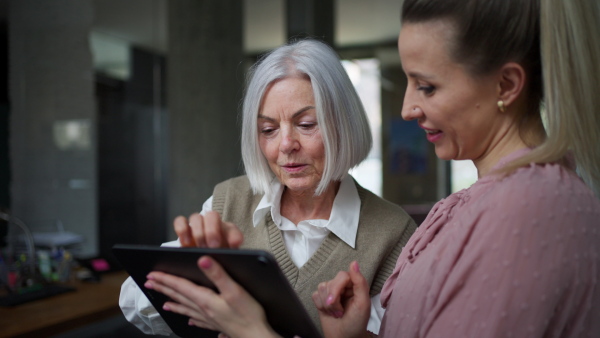 Two female colleagues in various age groups in office. Older manager as mentor for new female employee. Age diverse team concept.