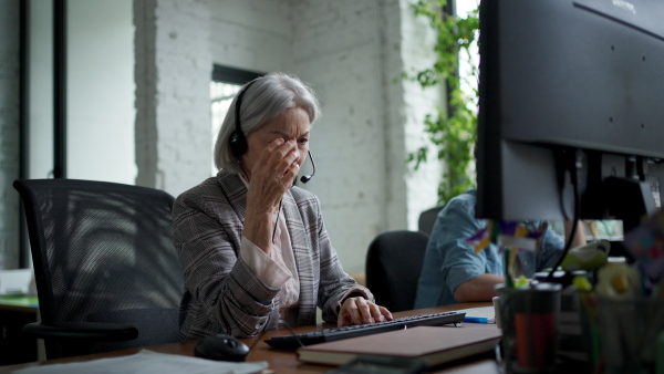 Young corporate worker with headset making phone call. Video of two colleagues in various age groups in office. Age diverse team concept.