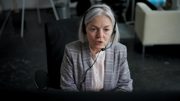 Senior corporate worker with headset making phone call. Call centre concept.