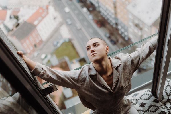 Top view of young unhappy woman with cancer sitting in window.