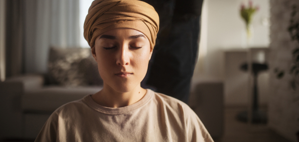 Young woman with cancer taking yoga and meditating in her apartment, banner. Strong female patient calming her mind with easy exercise. Concept of mental health and cancer. Cancer awareness day.