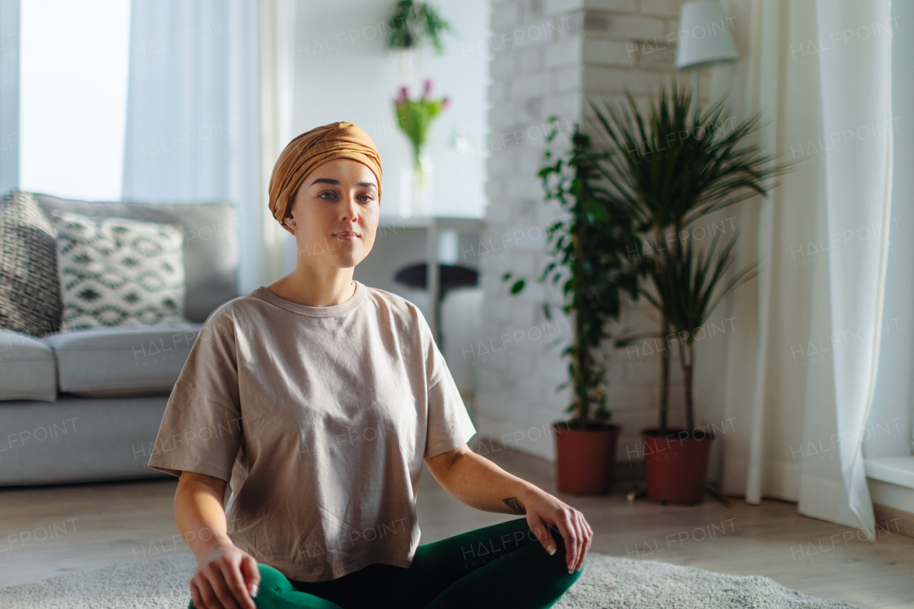 Young woman with cancer taking yoga and meditating in the apartment.