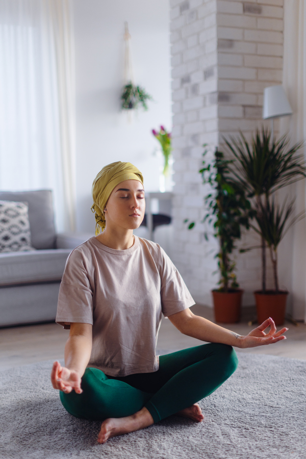 Young woman with cancer taking yoga and meditating in the apartment.