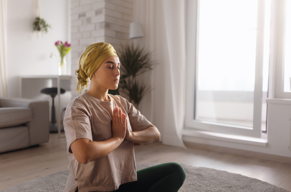 Young woman with cancer taking yoga and meditating in the apartment.