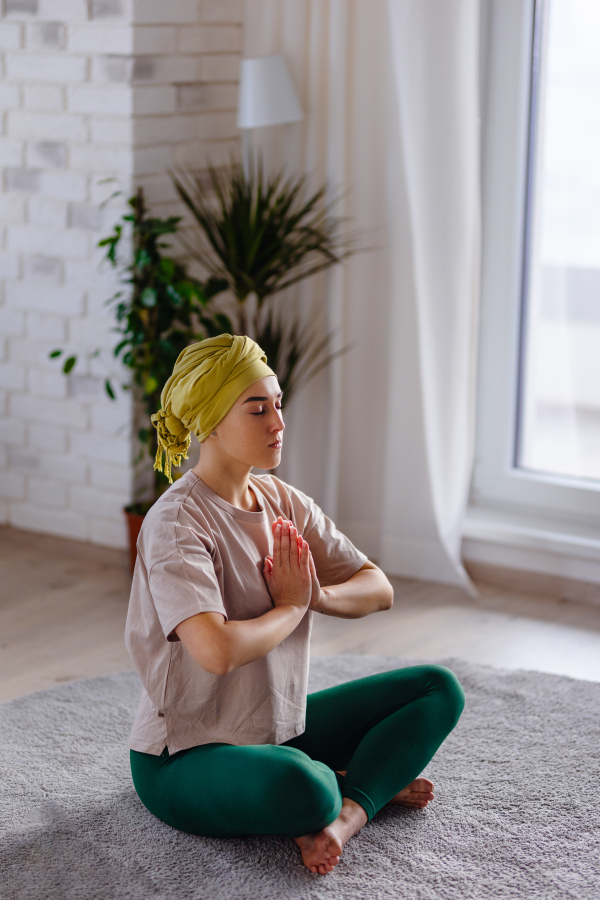 Young woman with cancer taking yoga and meditating in the apartment.