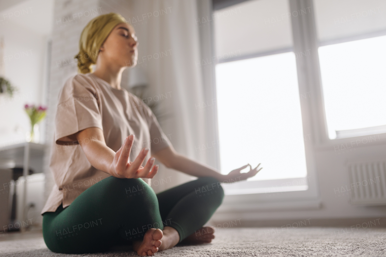 Young woman with cancer taking yoga and meditating in the apartment.