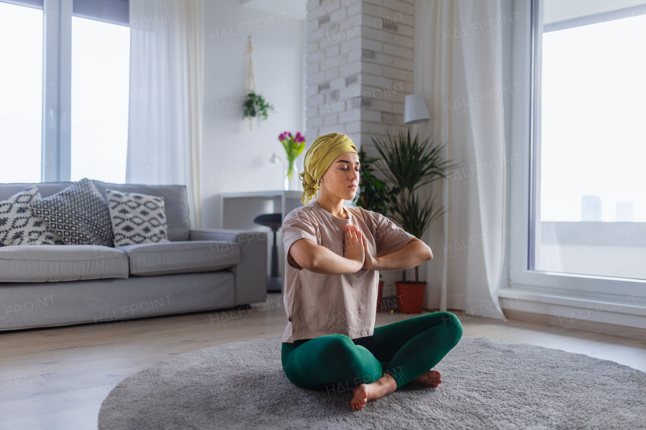 Young woman with cancer taking yoga and meditating in the apartment.