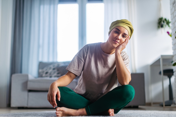 Young woman with cancer resting after taking yoga, in her apartment.