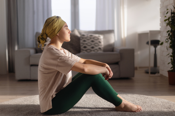 Young woman with cancer sitting after doing yoga in the apartment.