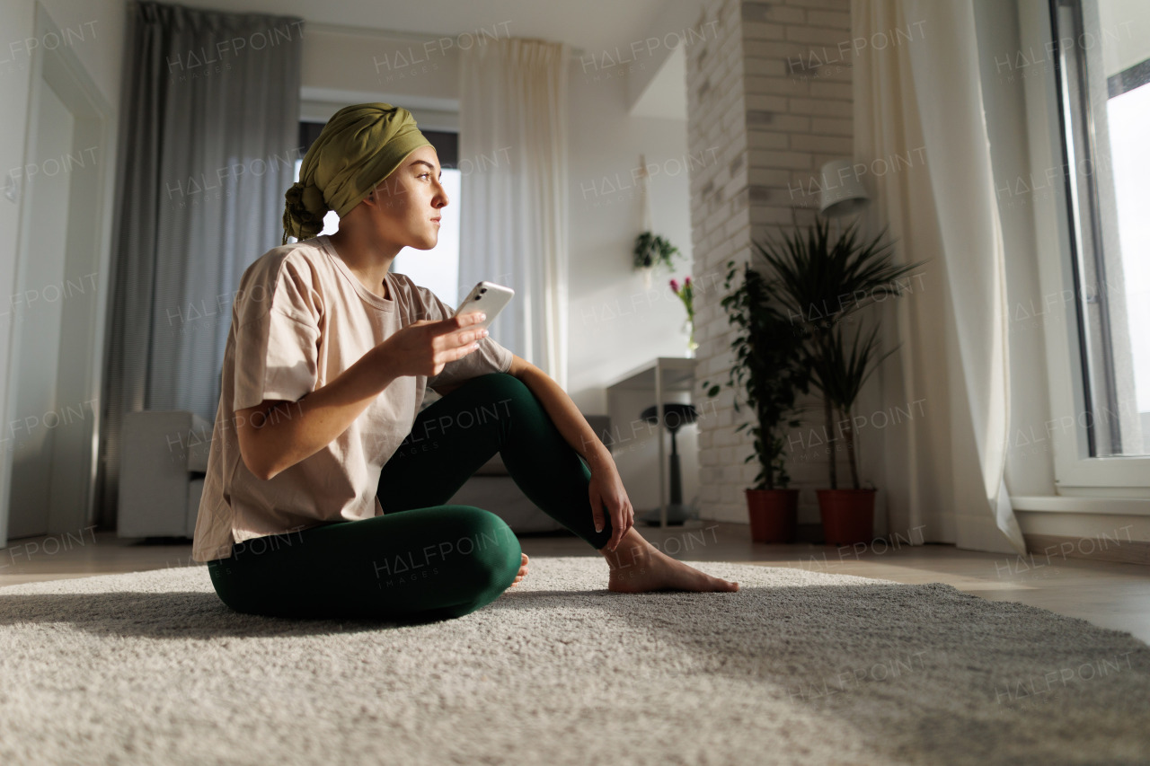 Young woman with cancer siting at home and scrolling a phone.