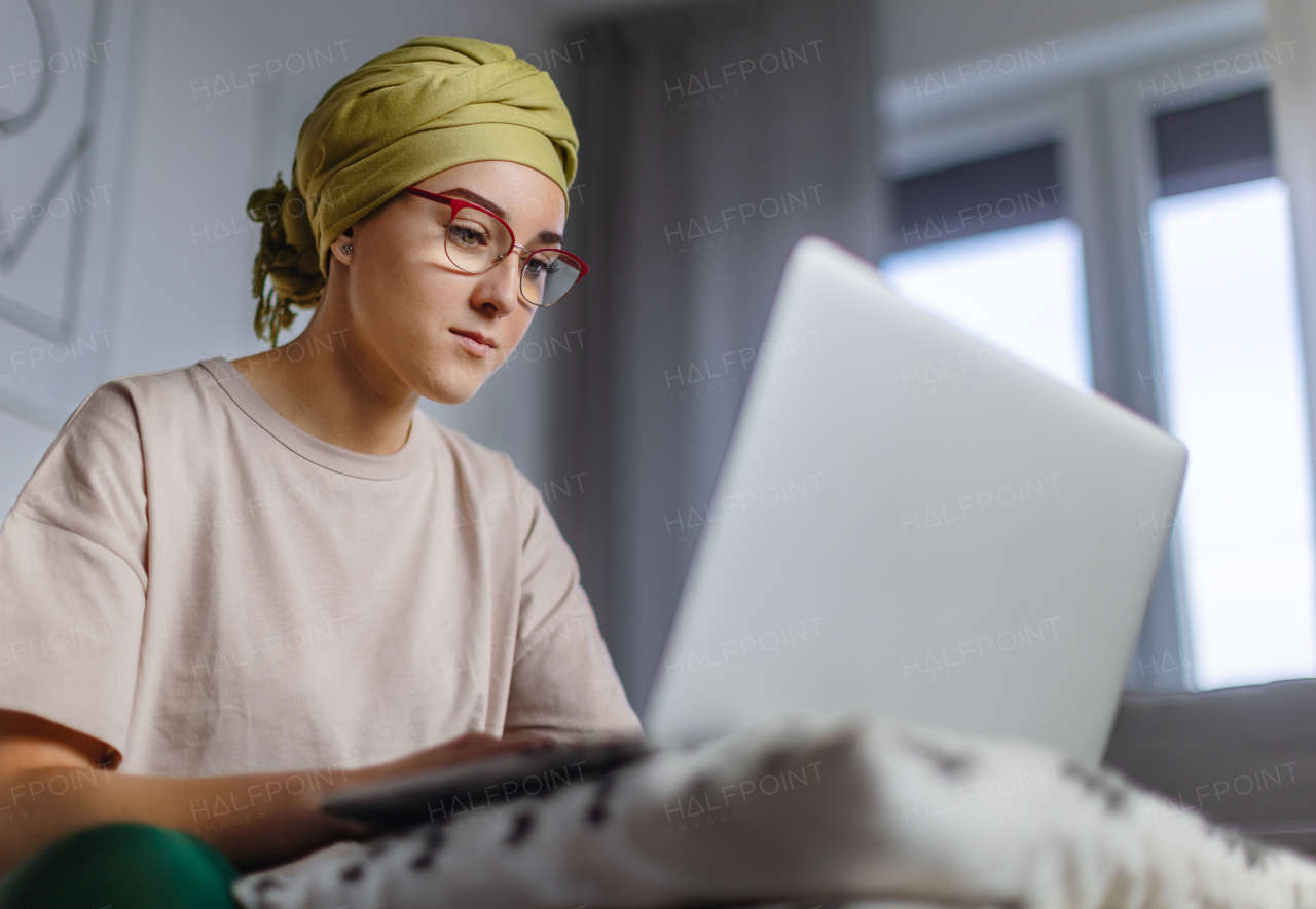 Young woman with cancer working on laptop in the apartment.