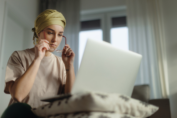 Young woman with cancer working on laptop in the apartment.