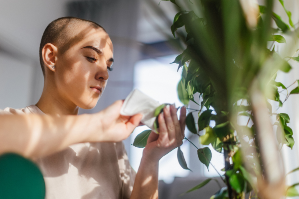 Young woman with cancer taking care of plants in the apartment.