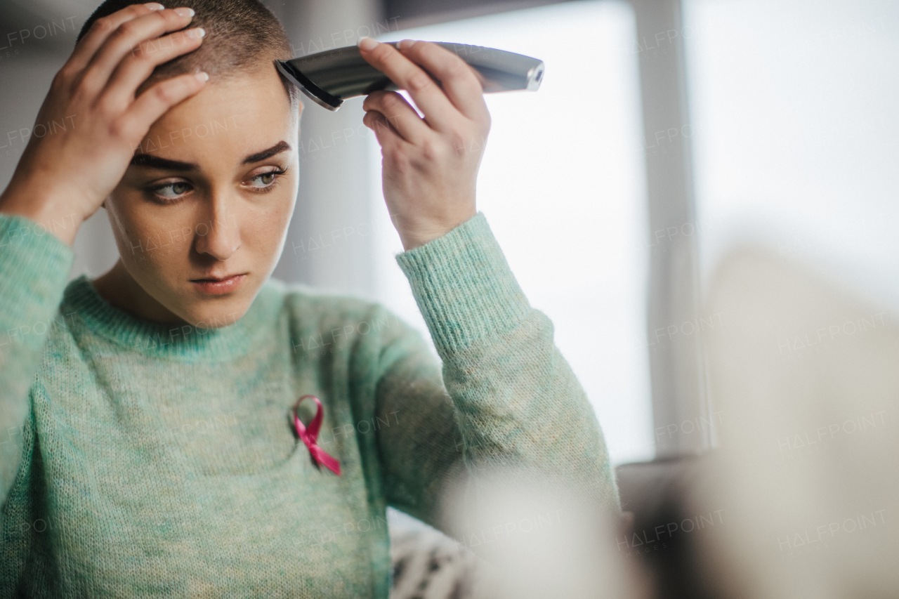 Young woman shaving her hair before chemotherapy. Cancer patient woman in bathroom shaving or trimming hair.