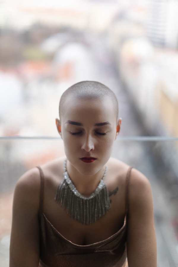 High angle view of young unhappy woman with cancer sitting in window.