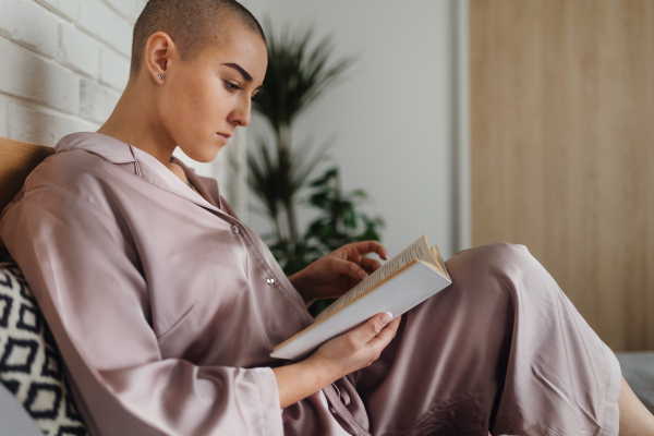 Young woman with cancer reading a book, cancer awareness concept.